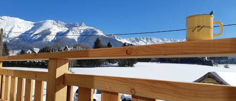 A wooden balcony with a yellow mug on the railing, overlooking a snowy mountain landscape.