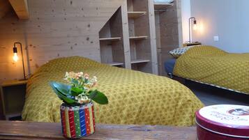 A room with a bed covered in a yellow patterned blanket, a small table with a colorful vase, and a red tin box.