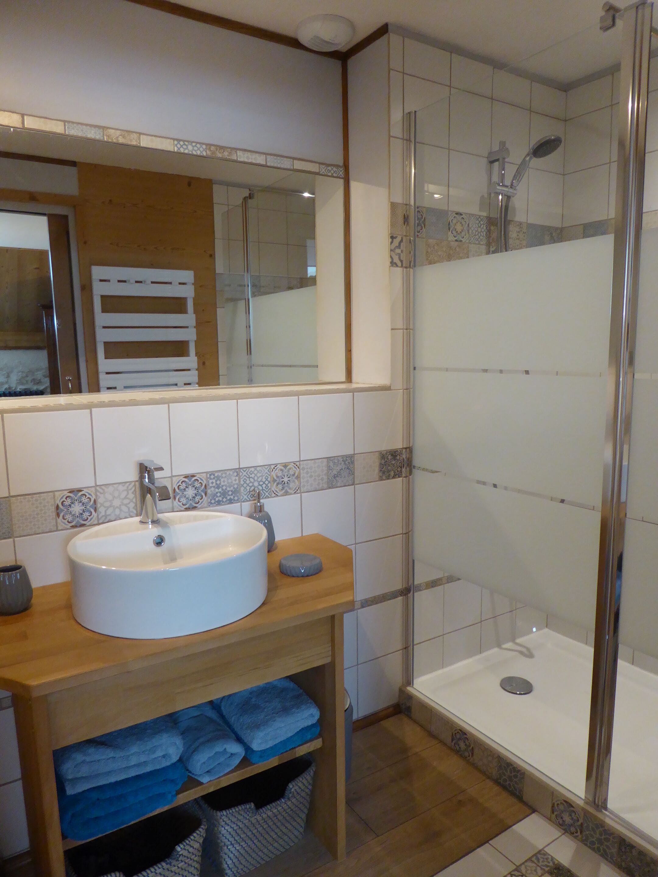 Un baño con lavamanos blanco, un espejo, ducha y repisa con toallas dobladas.