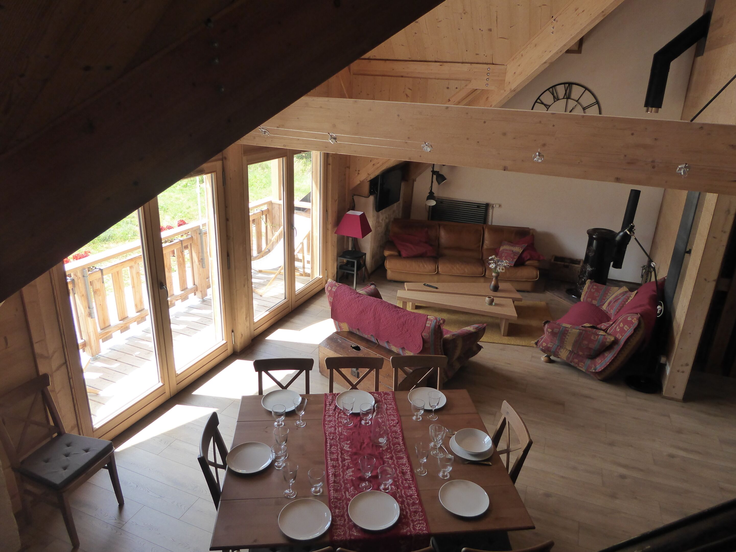 Un coin repas avec une table en bois dressée pour six personnes, un canapé et un escalier menant à une terrasse extérieure.