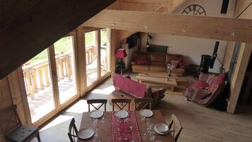 Un coin repas avec une table en bois dressée pour six personnes, un canapé et un escalier menant à une terrasse extérieure.