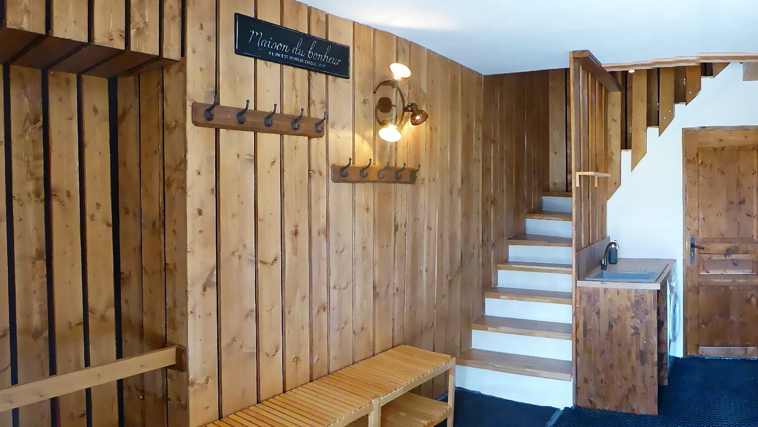 A wooden interior with a wooden bench, a staircase, and a sign that reads "Maison du bonheur".