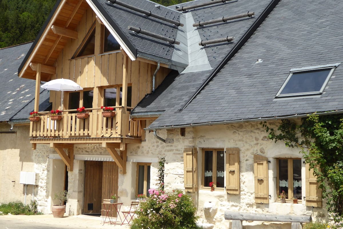 Un bâtiment rustique en pierre, doté d’un balcon en bois, d’une petite table et de chaises, ainsi que d’une plante en pot.