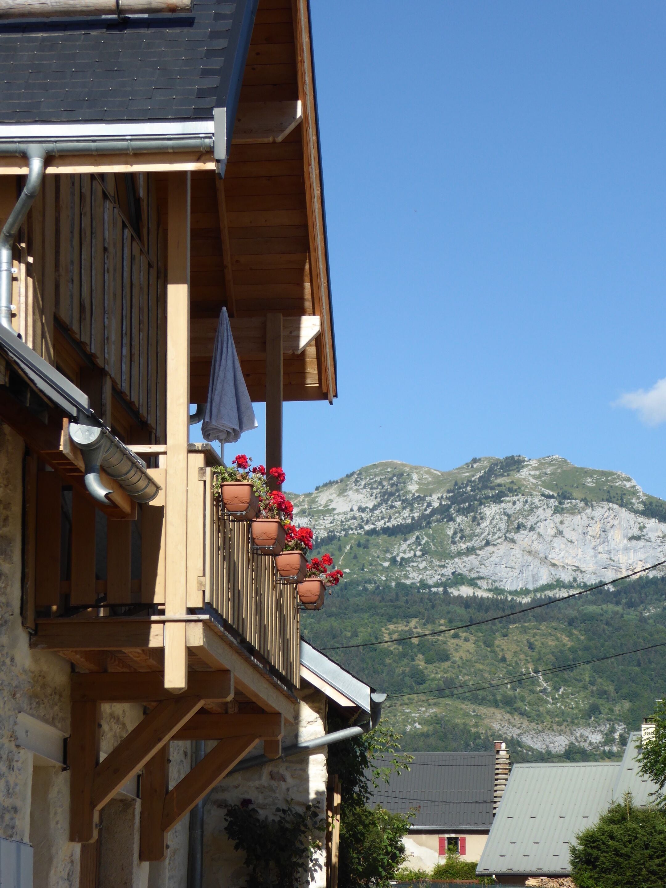 Ein Holzbalkon mit Blumentöpfen, bewölkter Himmel und ein Berg im Hintergrund.