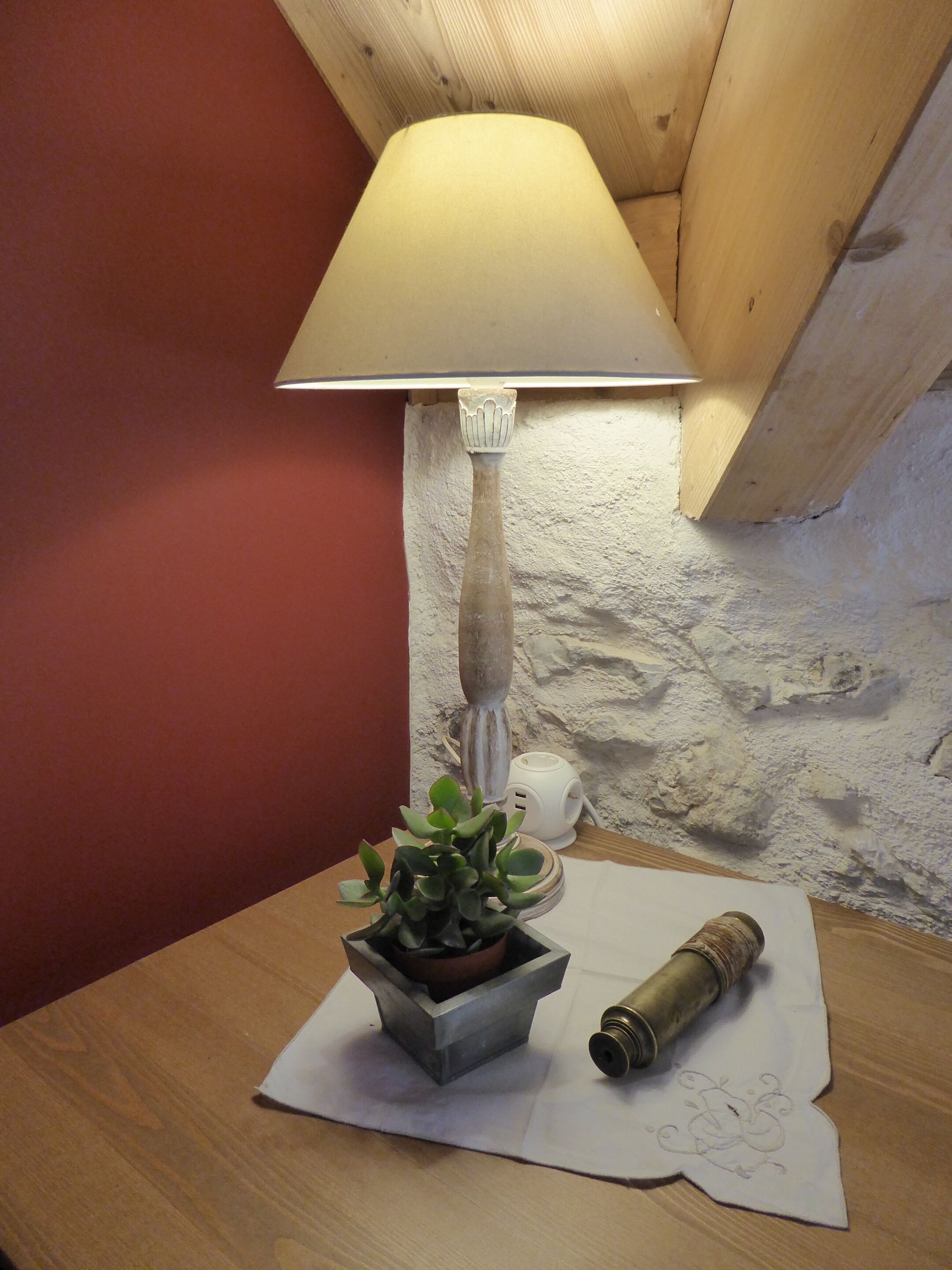 Een lamp met een witte kap, een potplant, een klein wit voorwerp en een opgerold voorwerp op een houten tafel.