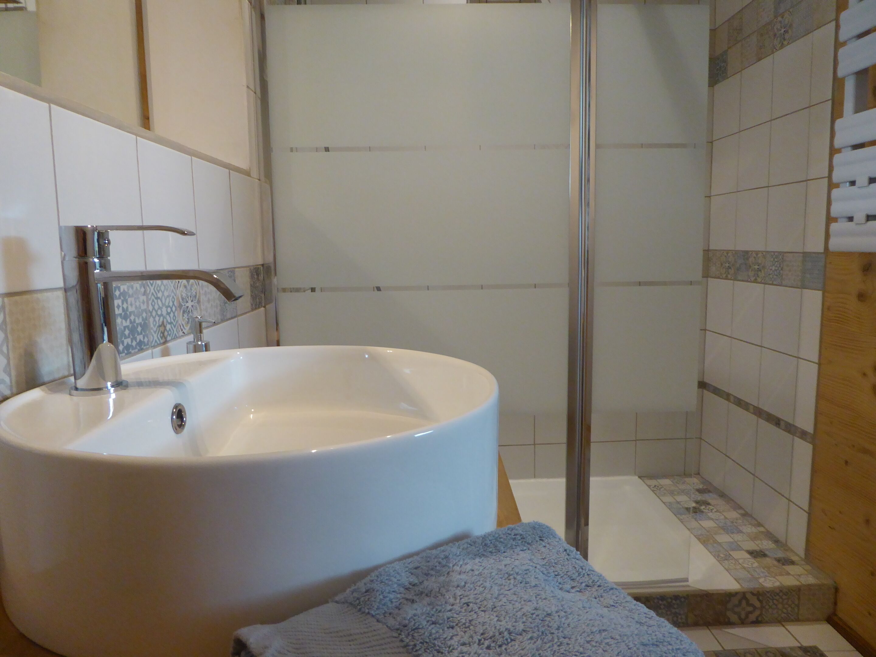 A bathroom with a large white sink, a glass shower enclosure, and a tiled shower area.