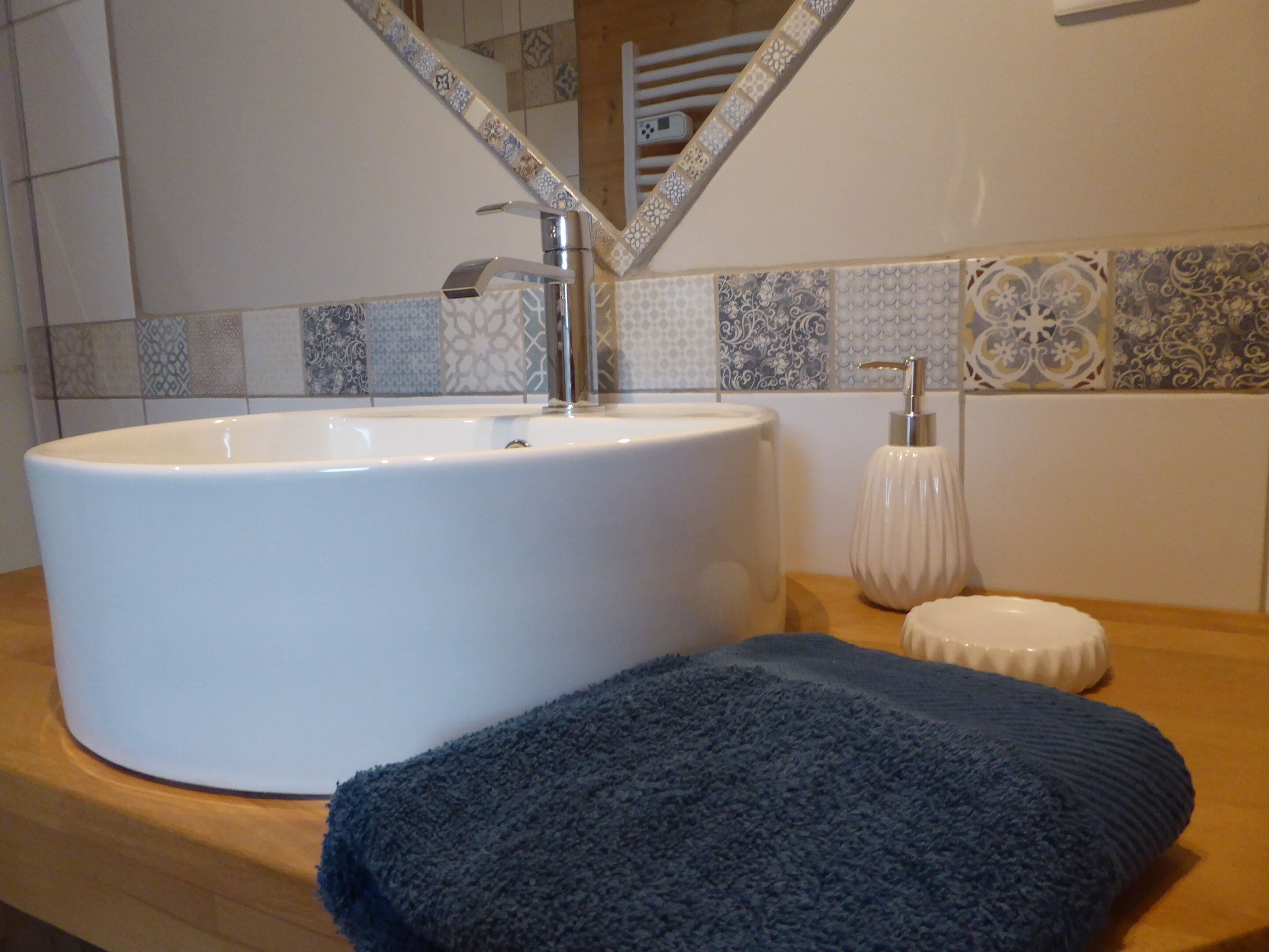Une salle de bain avec un grand lavabo blanc, une serviette et un distributeur de savon posés sur un comptoir en bois.