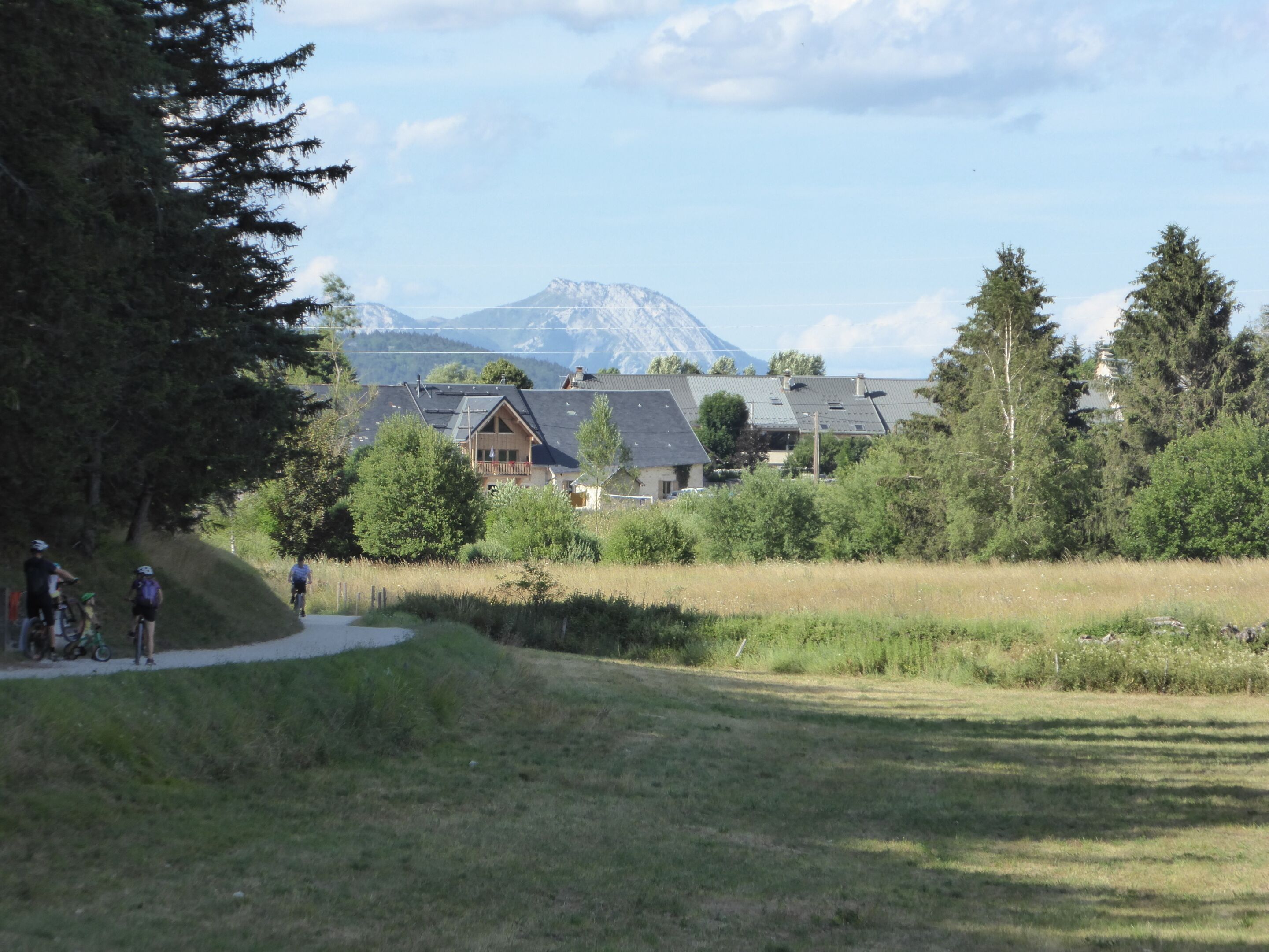 A rural setting with a mountain in the background, a pathway, and a building with a balcony.
