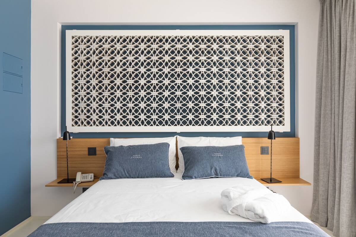 A neatly made bed with a white and blue color scheme, a decorative headboard, and a bedside table with a lamp and a phone.
