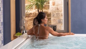 A person in a bathtub with a view of a stone wall and a plant outside. - Santa Caterina - Dimora sul mare (Polignano a Mare)