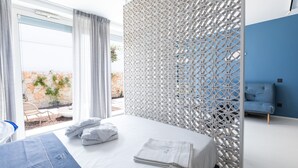 A modern hotel room with a large bed, a decorative white partition, and a view of an outdoor area with plants and a stone wall. - Santa Caterina - Dimora sul mare (Polignano a Mare)