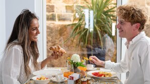 A dining table with breakfast items, a vase with flowers, and a view of a stone wall and plant. - Santa Caterina - Dimora sul mare (Polignano a Mare)