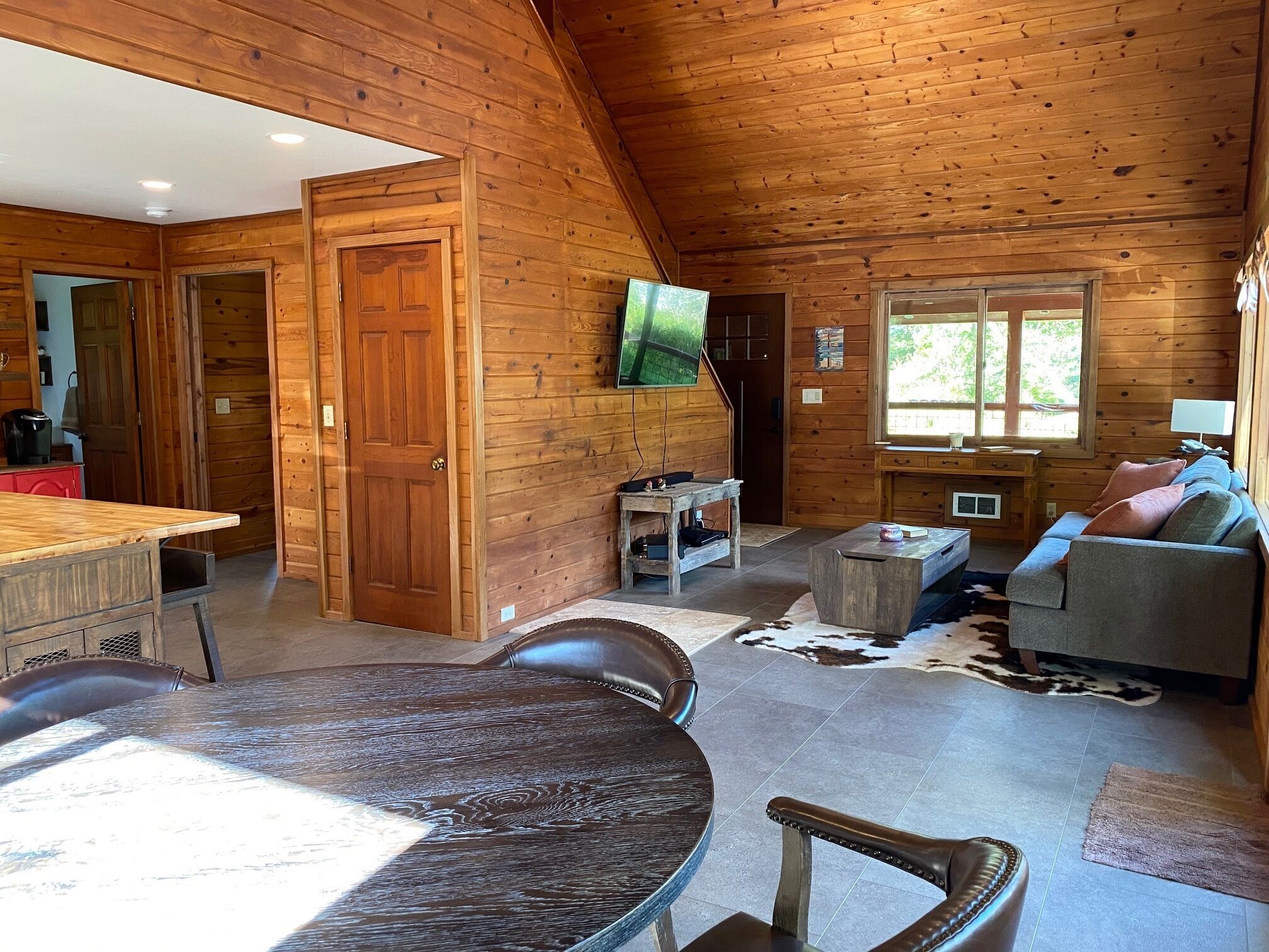 Ein gemütliches Blockhaushaus-Interieur mit Essbereich, Wohnzimmer mit Sofa und Fernseher sowie Holzboden.