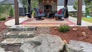 A covered outdoor seating area with stone steps leading to a fire pit, surrounded by a landscaped garden. - Treehouse and Gazebo with Fireplace close to the Beach (Nehalem)