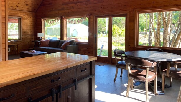A cabin with a wooden interior, a dining area with a table and chairs, and a sofa in the living area. - Treehouse and Gazebo with Fireplace close to the Beach (Nehalem)