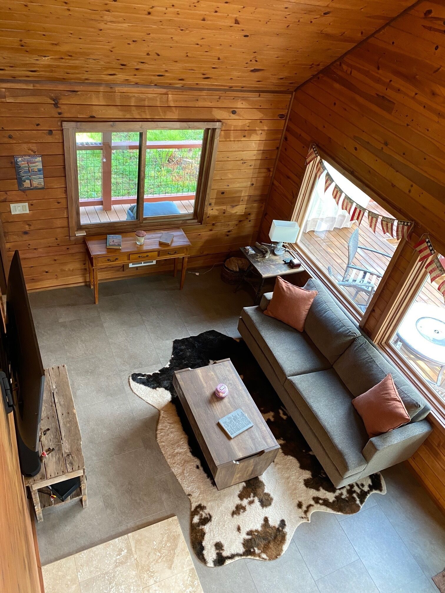 A cozy cabin interior with a wooden interior, a sofa, a table, and a window overlooking a garden.