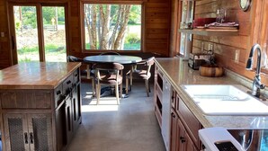 A modern kitchen with wooden cabinets, a central island, and a large window providing a view of the outdoors. - Treehouse and Gazebo with Fireplace close to the Beach (Nehalem)