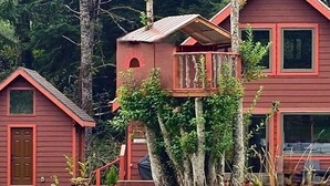 A red wooden cabin with a small balcony attached to a tree. - Treehouse and Gazebo with Fireplace close to the Beach (Nehalem)