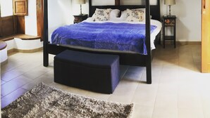 Uma cama de dossel com um cobertor azul, duas mesas de cabeceira com luminárias, teto de madeira e um pequeno tapete no chão.