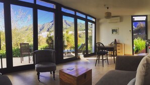 Uma sala de estar ampla com grandes janelas, uma mesa de centro de madeira e um espaço de jantar com cadeiras e uma mesa.