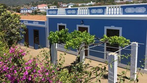 Um edifício azul com varandas brancas, rodeado por vegetação e montanhas ao fundo.