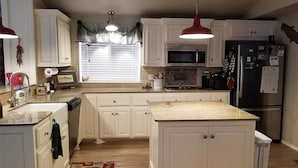 Une cuisine avec des meubles blancs, un îlot central, un four à micro-ondes, un réfrigérateur et des luminaires suspendus.