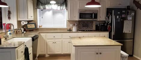 Cocina con alacenas blancas, una isla central, microondas, refrigerador e iluminación colgante.