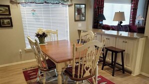 Un coin repas avec une table en bois et quatre chaises, un comptoir de cuisine et une fenêtre avec des stores.
