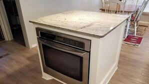 Une cuisine compacte dotée d’un four et d’un micro-ondes encastrés, d’un plan de travail en bois et d’un coin repas avec des chaises.