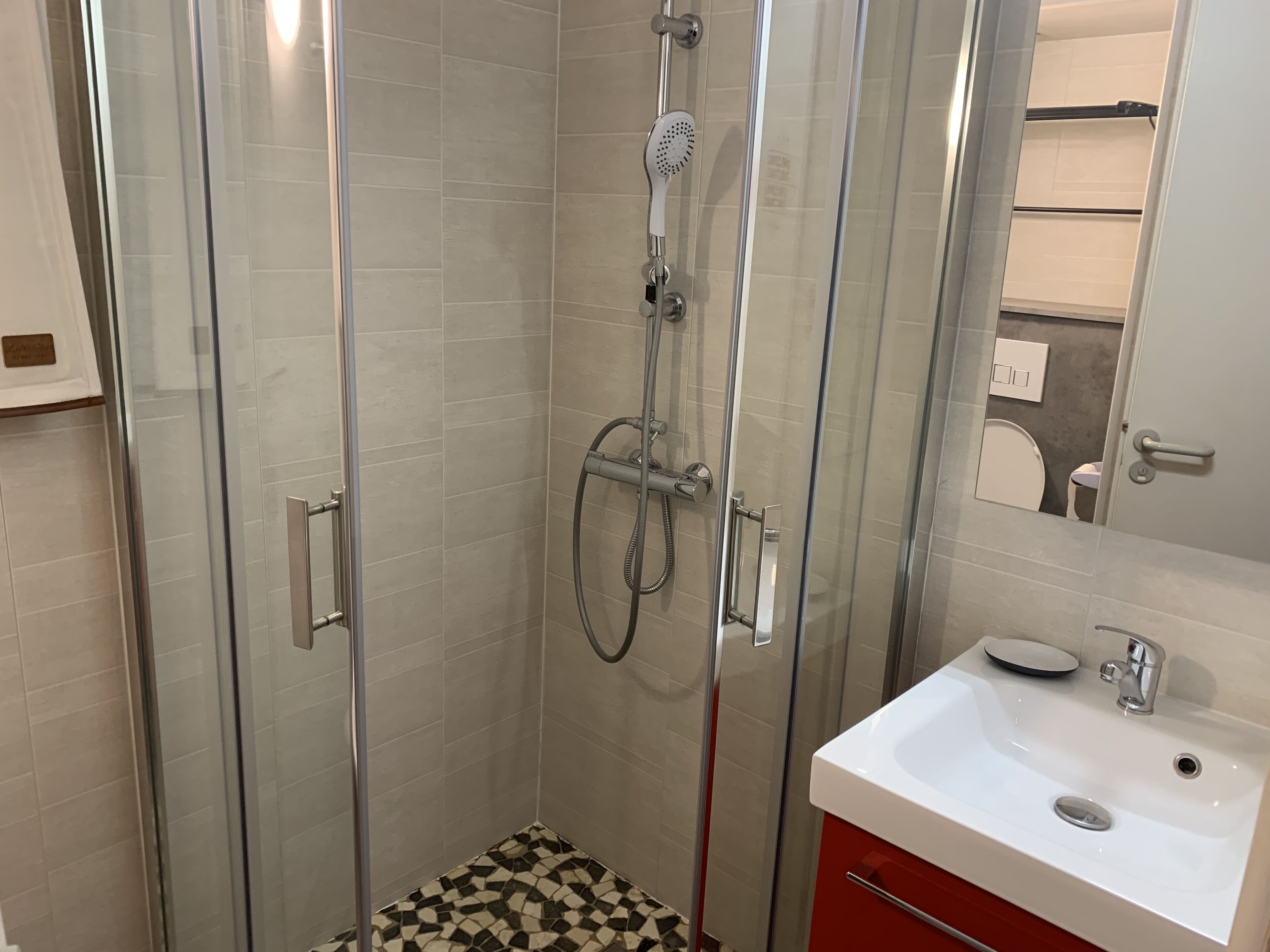 Une salle de bain moderne avec une douche à parois de verre, un lavabo blanc et un meuble rouge.