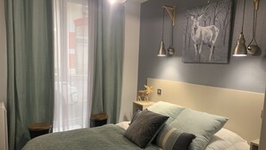 A neatly made bed with a green quilt, a headboard with a painting of a deer, and a bedside table with a lamp and a decorative item.