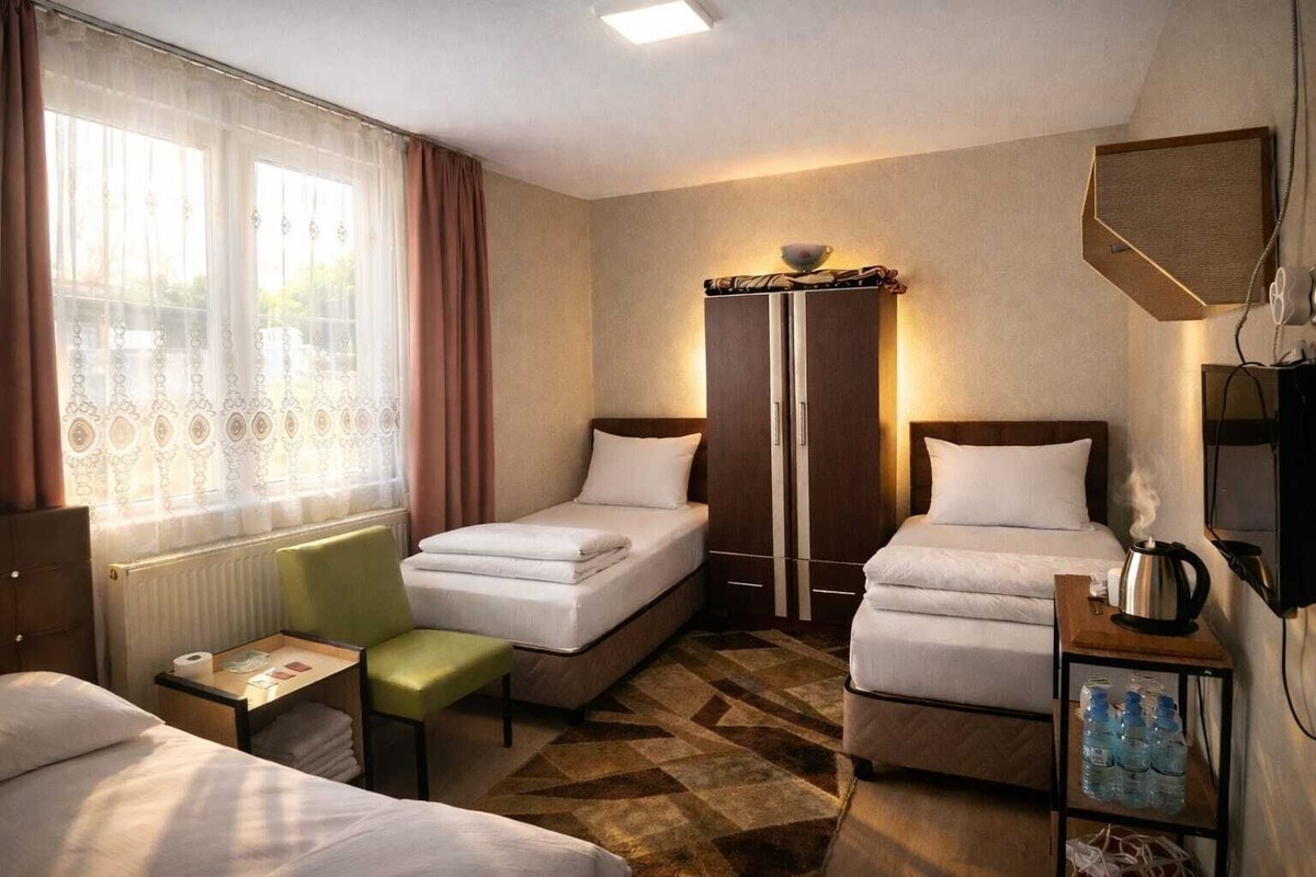 A hotel room with two single beds, a small table with a chair, a wardrobe, a radiator, and a television.