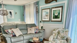 A living room with a grey sofa, a patterned armchair, a round coffee table, and a ceiling fan.
