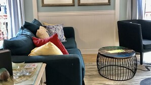 A living room with a blue sofa, two framed pictures, a wooden fish decoration, a round coffee table, and a patterned rug.