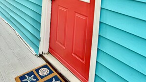 A red door with a window, a lobster decoration, and a doormat with starfish and shells.