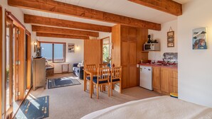 A compact kitchen with wooden cabinets, a dining area with a table and chairs, and a small refrigerator. - Pointers - Akaroa Holiday Home (Akaroa)
