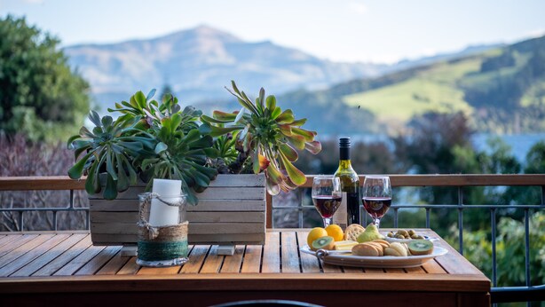 A wooden table with a potted plant, a candle, a wine bottle, and a plate of food. - Pointers - Akaroa Holiday Home (Akaroa)