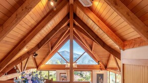 A wooden interior with a high ceiling and a large window overlooking mountains. - Pointers - Akaroa Holiday Home (Akaroa)