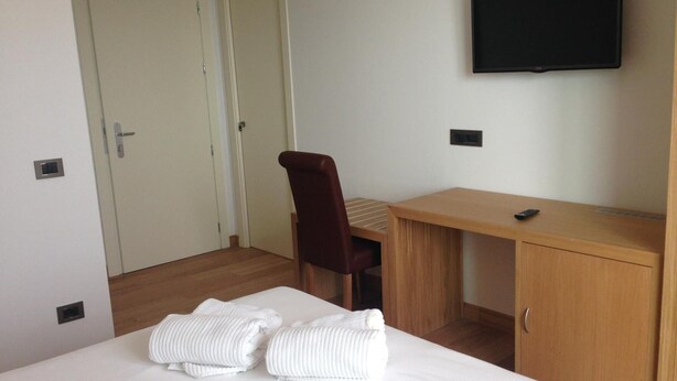A hotel room with a bed, a desk, a chair, a TV, and two doors.