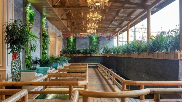 Una terraza de madera con bancos, una araña y plantas verdes a lo largo de las paredes.