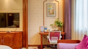 Habitación de hotel con televisión, mueble de madera, escritorio con silla y cama con almohada morada.