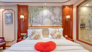 Habitación de hotel con una cama grande, un cojín rojo con forma de corazón, una pared con un mural de temática natural y una zona de ducha de vidrio.