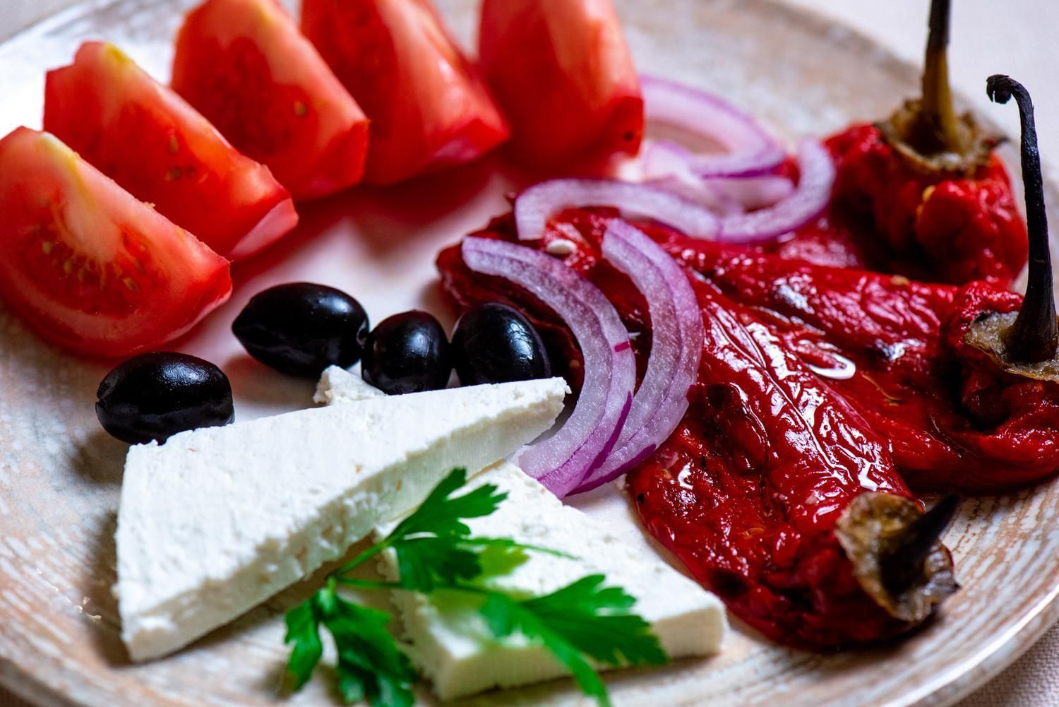 A plate with sliced tomatoes, red onions, black olives, and a wedge of cheese, garnished with parsley.