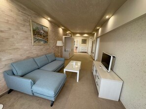 A modern living room with a blue sofa, a white coffee table, and a TV on a cabinet. - Siena Palace (Primorsko)