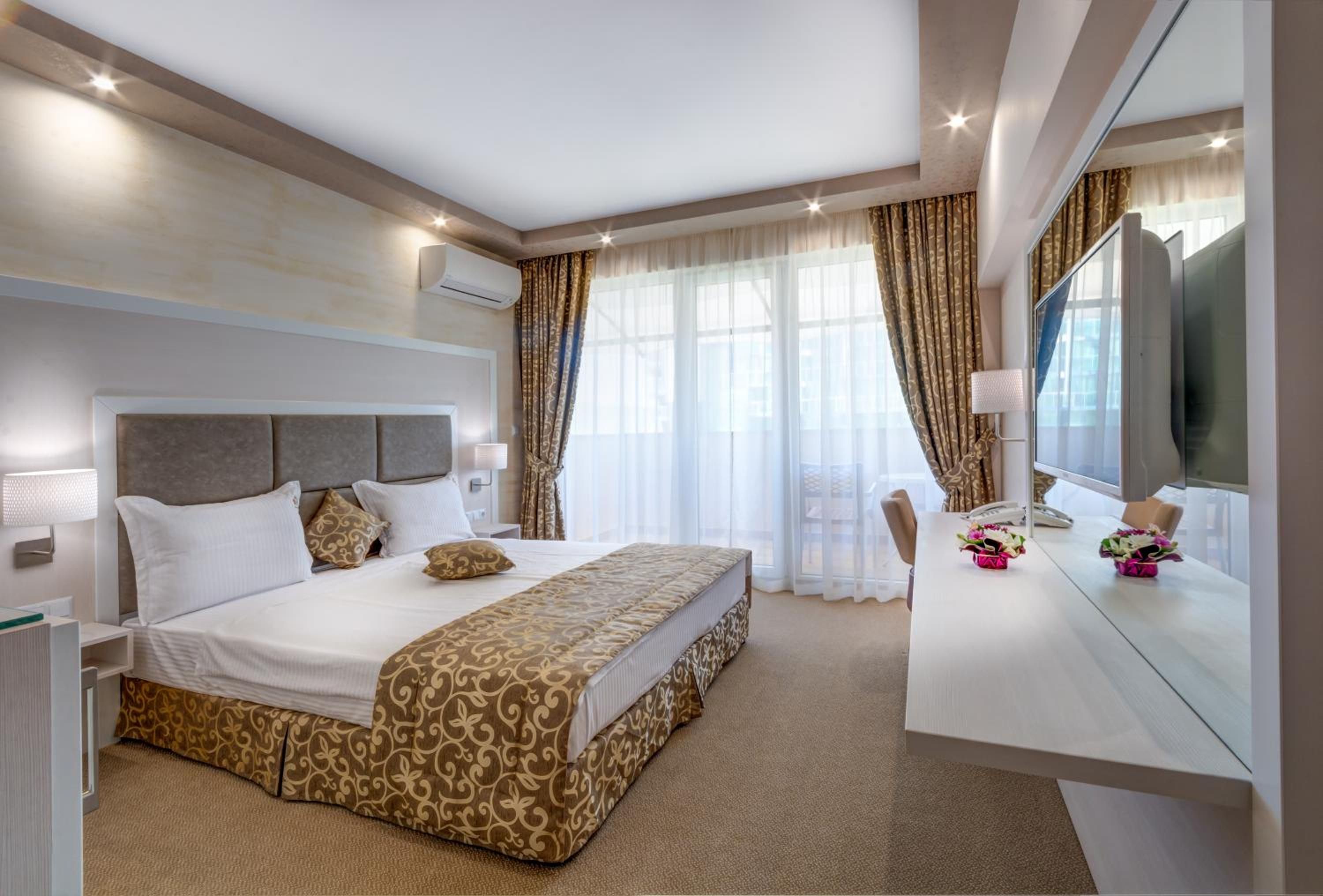 A modern hotel room with a large bed, a desk with a mirror, and a television.
