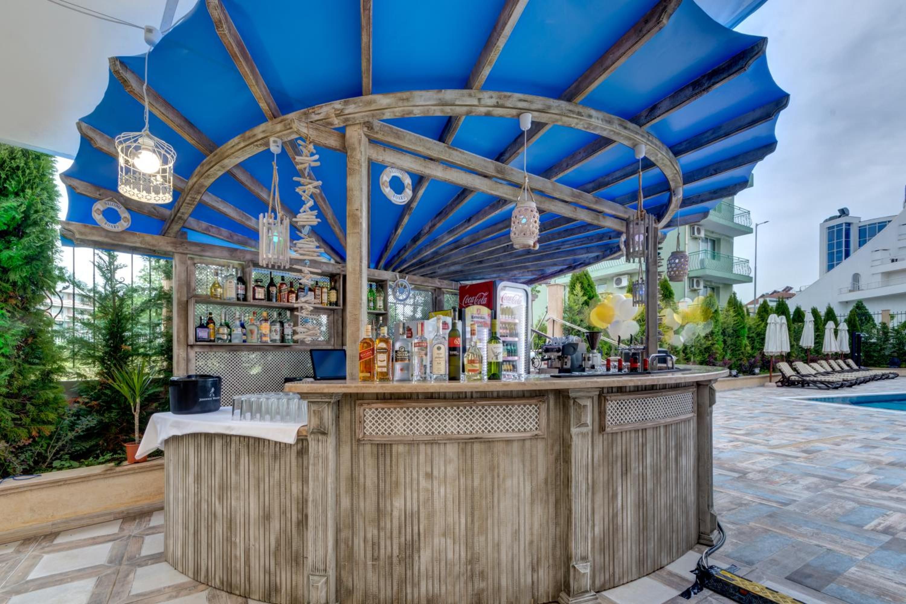 Una zona de bar con mostrador de madera, estantes llenos de botellas y un toldo azul.