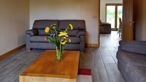 Una sala de estar con un sofá gris, una mesa de centro de madera y un jarrón con flores.
