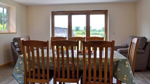 Un comedor con una mesa dispuesta para seis personas, sillas de madera, un sofá gris y una ventana con vistas a zonas verdes.