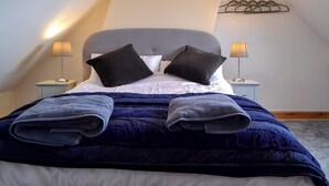 Una cama bien hecha con edredón azul oscuro y dos almohadas, dos lámparas de noche y un perchero de pared.