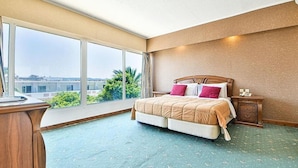 Ein Hotelzimmer mit einem großen Bett, einem Nachttisch und Blick auf die Stadt durch große Fenster.
